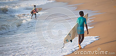 Kovalam, Chennai, Tamilnadu, India - â€Žâ€ŽAugust 9th â€Ž2021: Small Indian boy surfer carrying surfboard and walking on the beach Editorial Stock Photo